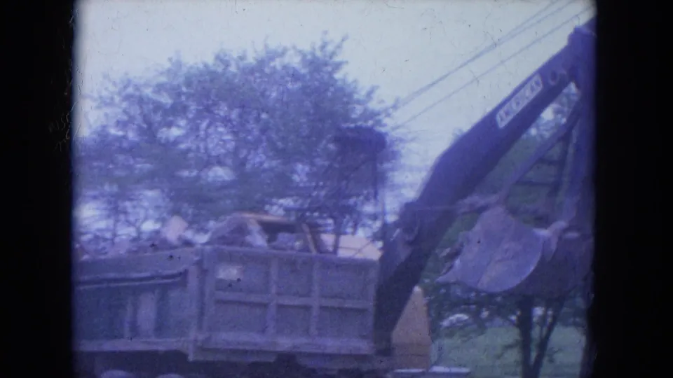 The excavator arm extends over a dump truck during debris loading in the Louisville construction scene, seen through faded 8mm color.