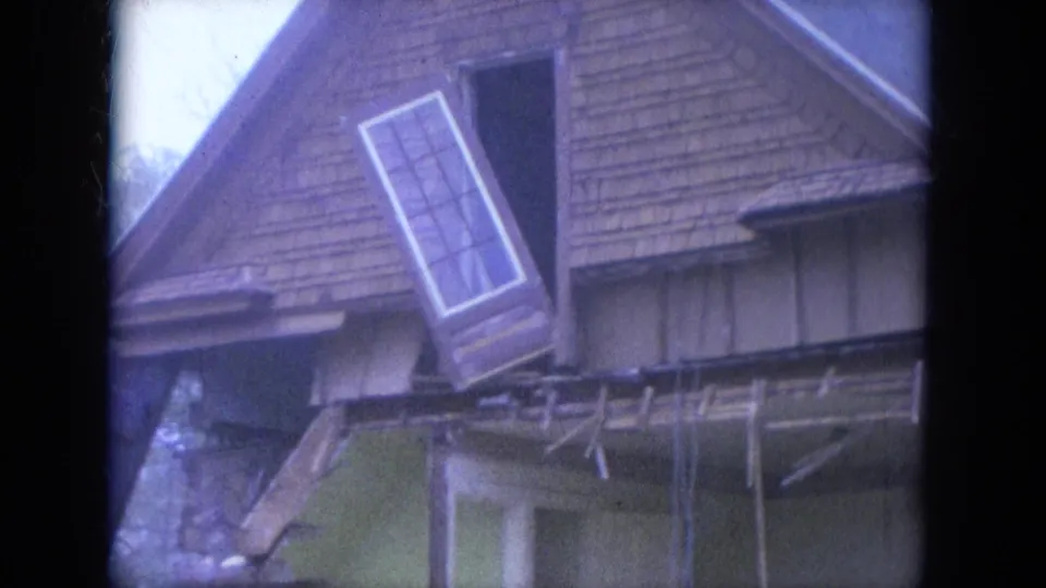 1965 Louisville frame with the loose window or door panel still hanging from the damaged upper story beneath a steep shingled roof.