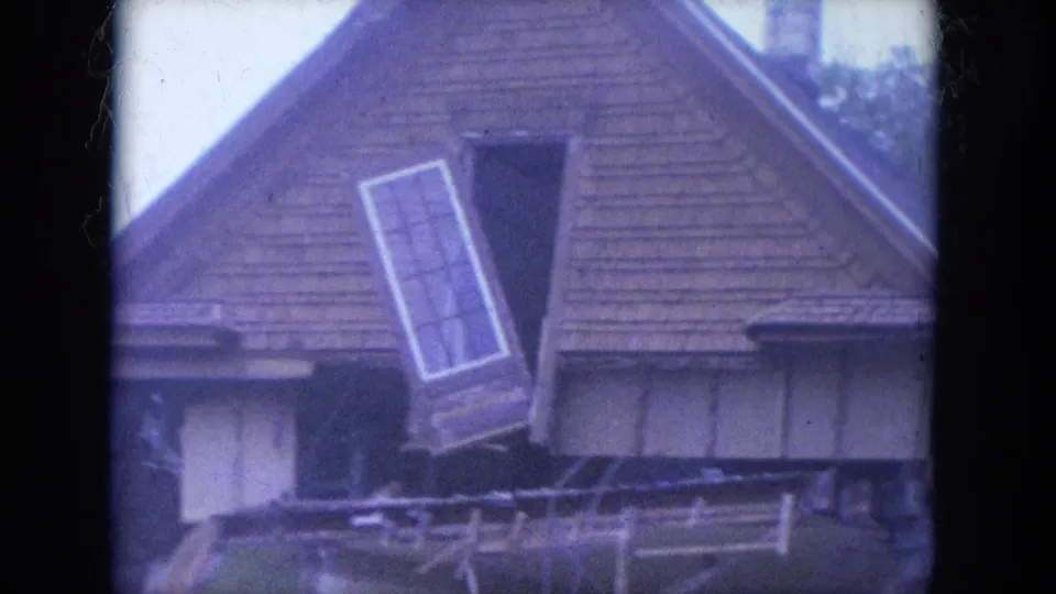 A soft 8mm frame from Louisville in 1965 shows the damaged upper story, angled window assembly, and exposed framing on a wood-sided house.