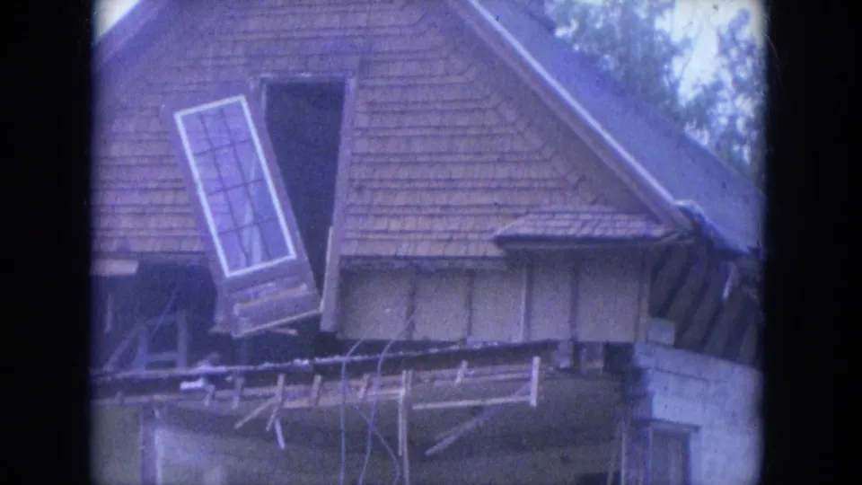 The final 1965 Louisville frame holds on the damaged wood-sided house, with the loose upper window assembly and broken roofline material visible.