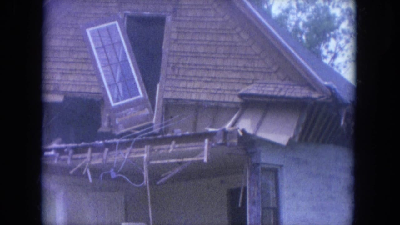 1965 Louisville home-movie frame showing a shingled house exterior as a loose window frame tilts outward above a damaged porch during demolition.