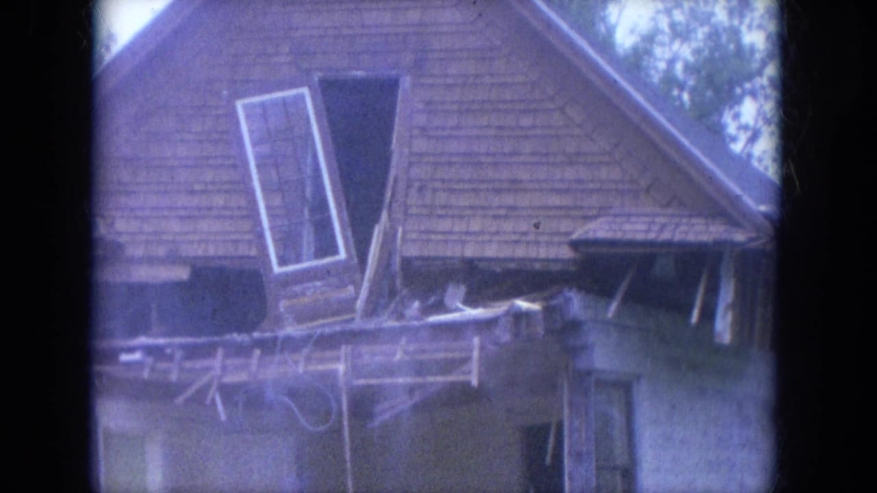 House roof and upper wall with window frame partly detached during demolition.