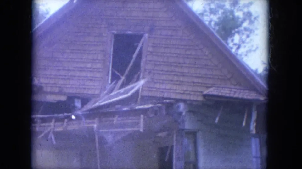 1965 Louisville home-movie frame showing a house section collapsing, with roof material, porch framing, and loose boards shifting downward.
