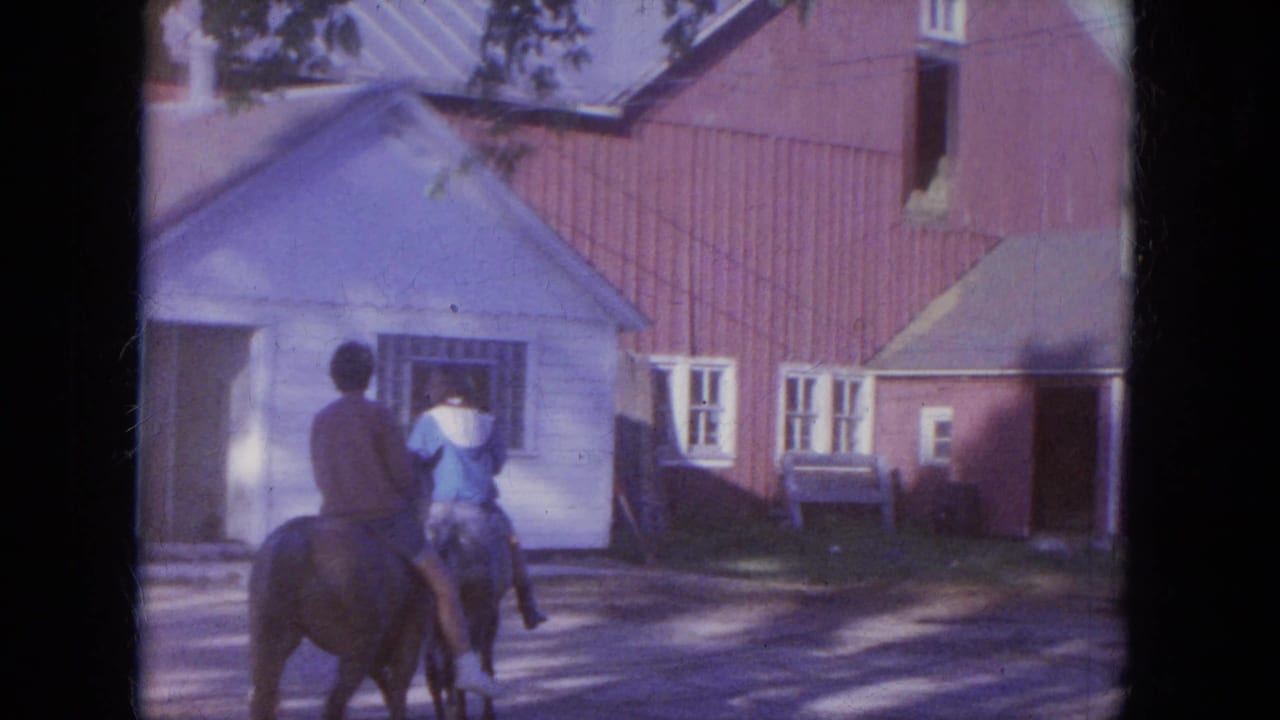 Two riders on horseback move past a white outbuilding and red barn-like structure in 1965 Louisville-area 8mm home-movie footage.