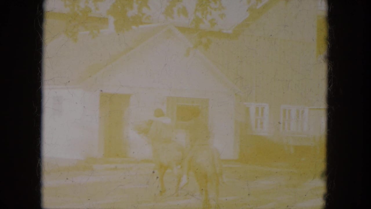 A bright, faded 8mm frame shows the horseback riders near rural buildings, with details partly washed by exposure.