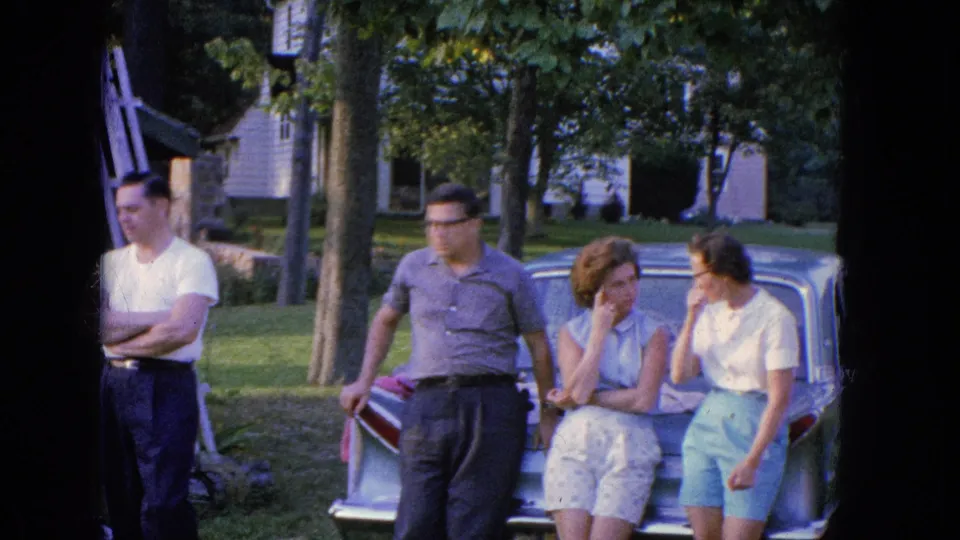 Four adults gather beside a parked car in Manchester, New Hampshire in 1965, with two women seated on the trunk and two men standing nearby.