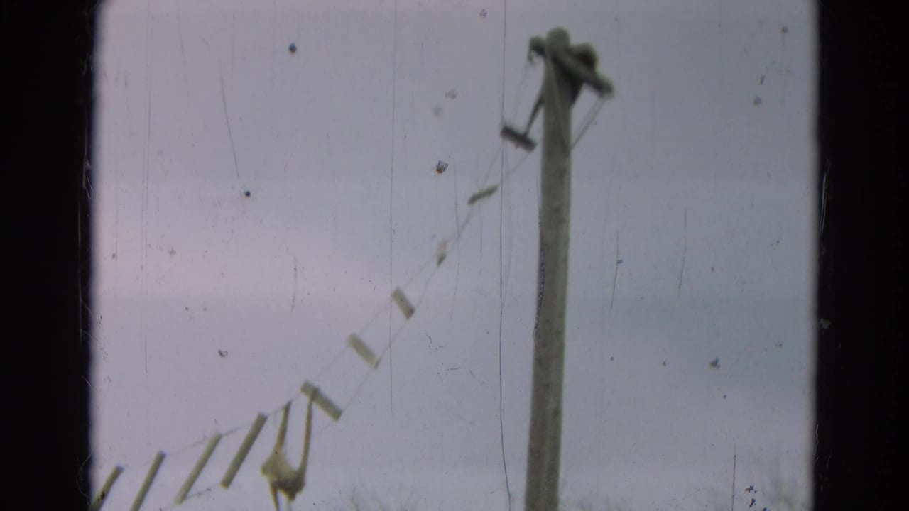 Tall wooden post with rope and suspended plank bridge against a pale sky.