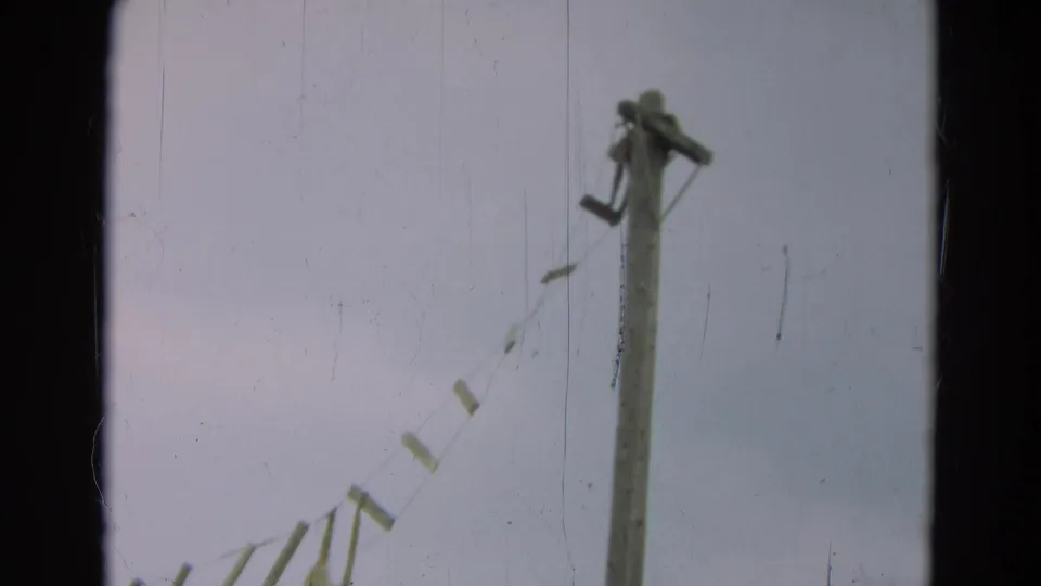 1965 Omaha home-movie view of rough bridge slats and rope supports leading toward a tall wooden post.