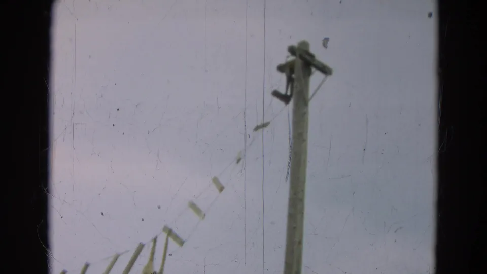 1965 Omaha frame showing the rope-and-plank bridge structure, with a tall post and weathered slats visible against the sky.