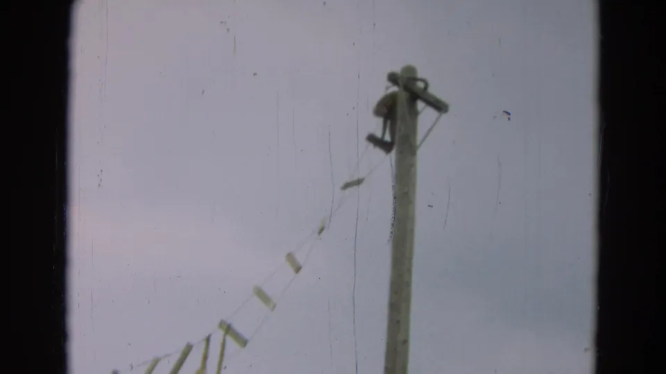 1965 Omaha 8mm frame showing a wooden utility pole and a diagonal hanging line against an overcast sky.