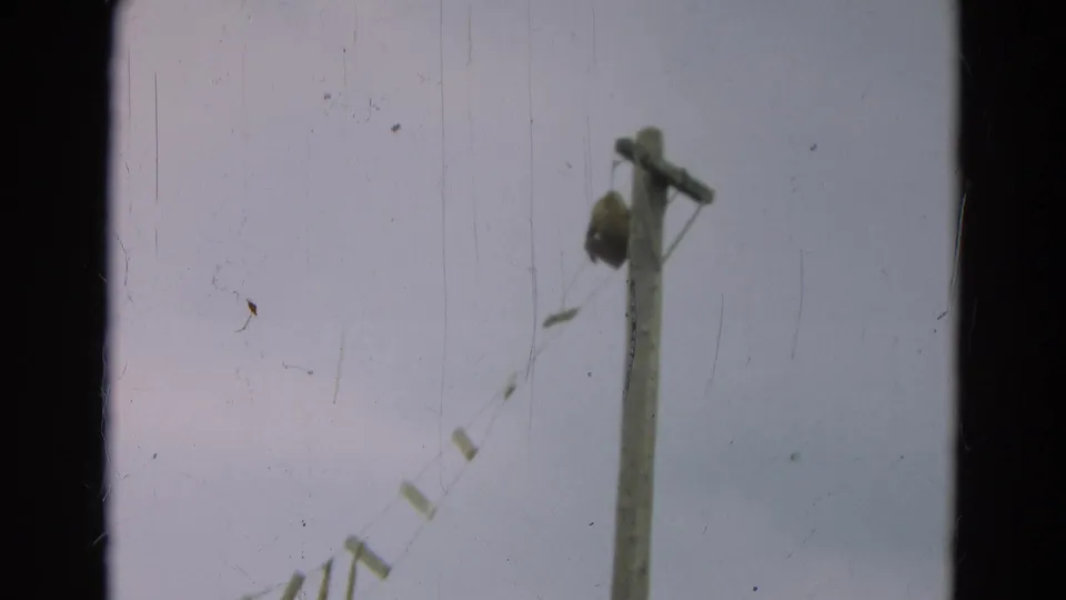 1965 Omaha home-movie frame with a wooden utility pole, suspended line, pale sky, and visible film wear.