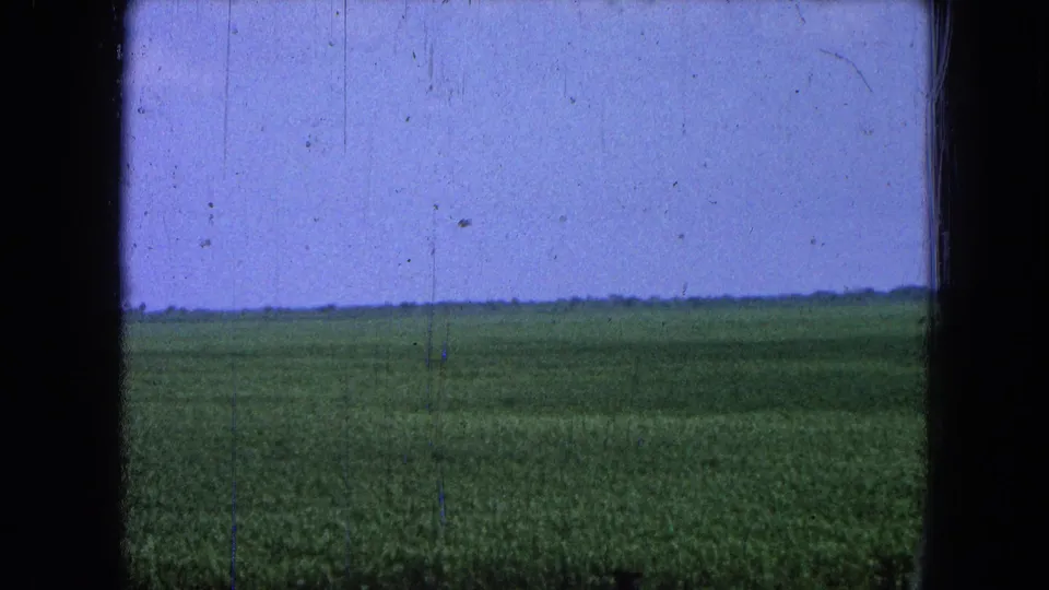 A steady 1965 8mm rural view in Pueblo, Mexico, with green grassland reaching toward a distant flat horizon.