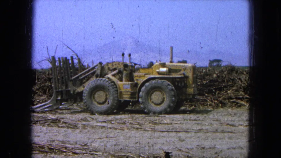 Yellow loader-like farm vehicle in a Pueblo, Mexico field, with large tires, crop debris, blue sky, and 8mm film borders.