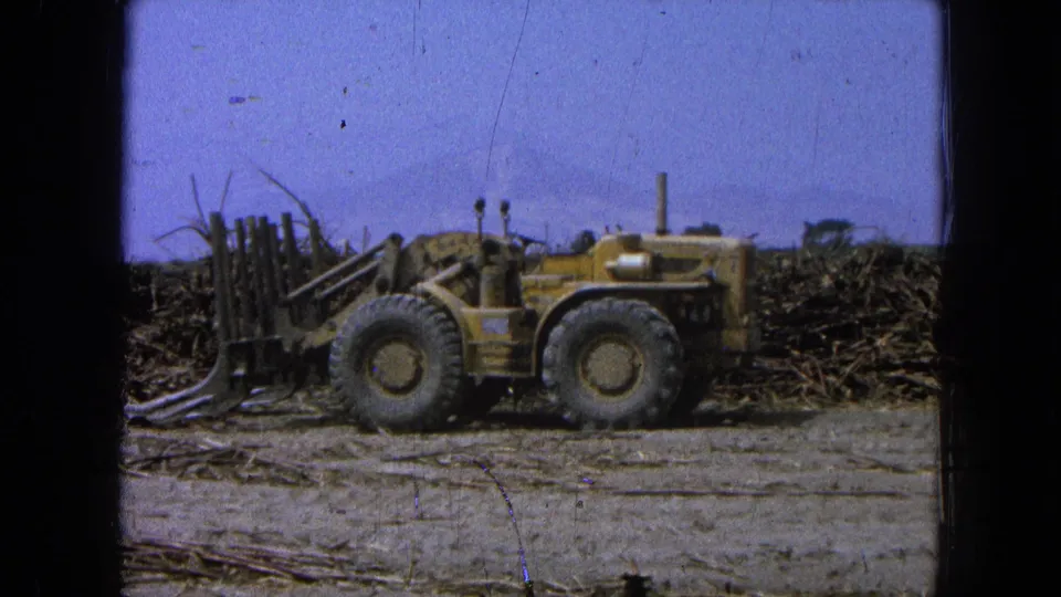 1965 Pueblo, Mexico frame of a yellow front loader viewed from the side, positioned near scattered brush and debris.