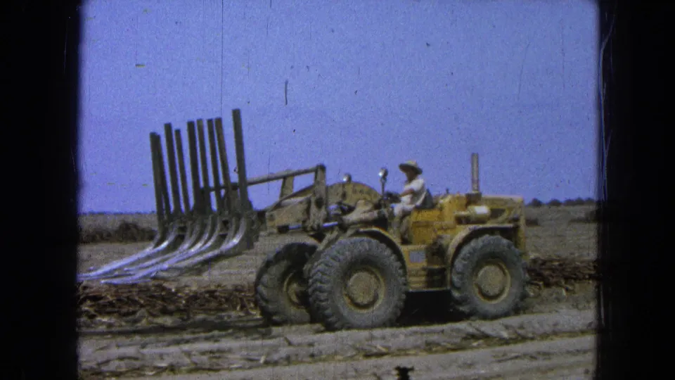 1965 Pueblo, Mexico frame showing a driver on a yellow loader with the forked attachment lifted over debris.