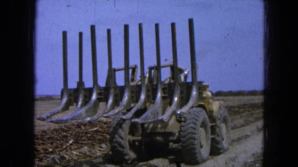 1965 Pueblo, Mexico footage shows a yellow tractor with tall soil tines moving through a dry rural field.
