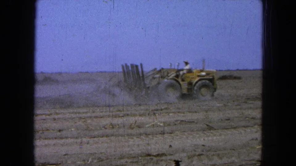 1965 Pueblo, Mexico footage of a tractor operator clearing a dry field as dust trails behind the vehicle.