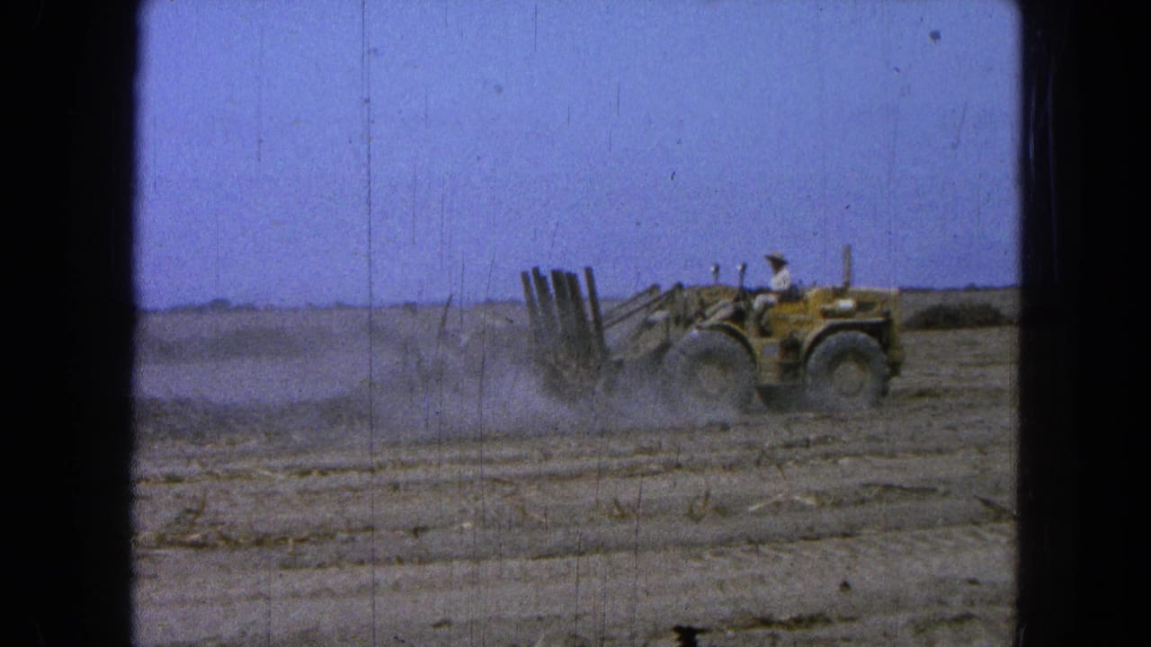 Tractor and operator at the right side of a dusty open field.
