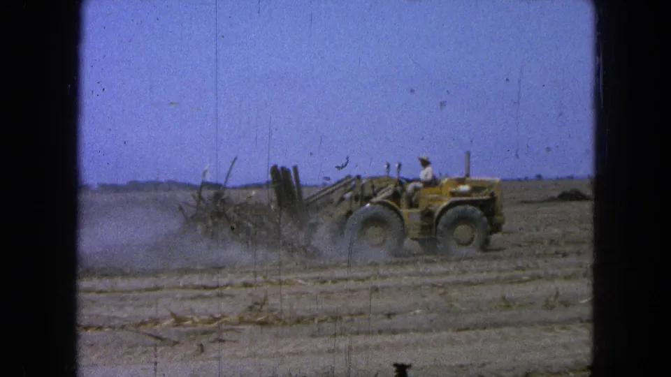 1965 Pueblo, Mexico 8mm frame showing a man operating a yellow front-end loader in a dusty open field.