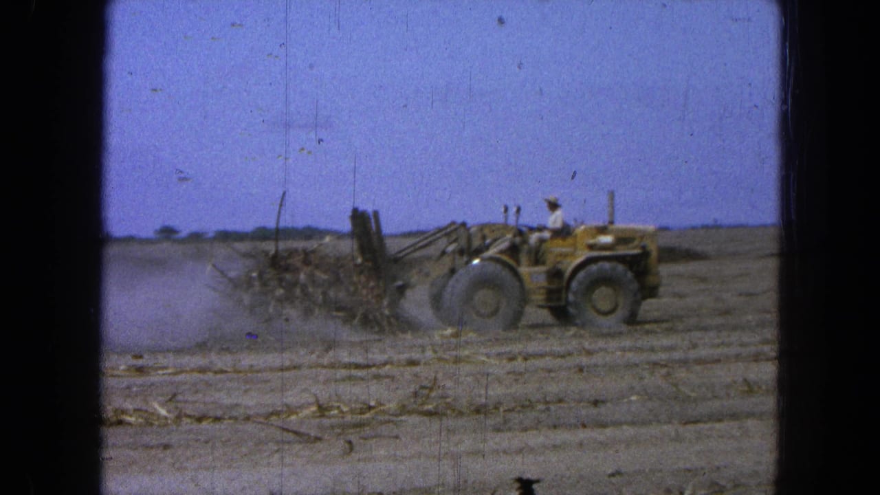Front-end loader continues across the field with dust trailing behind its blade.