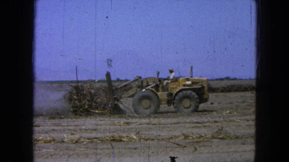The yellow loader continues pushing logs and branches across dry ground in Pueblo Mexico, 1965.