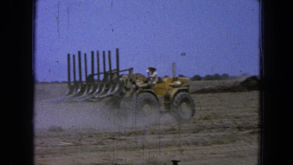 The yellow loader continues through the dry agricultural field in Pueblo, Mexico, with the worker visible and dust trailing near the attachment.
