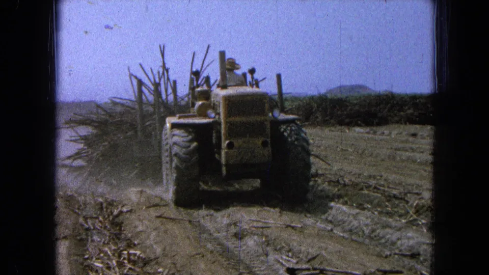 8mm home-movie frame showing the tractor from behind as it pulls vegetation through a dry field in the 1965 Mexico clip.