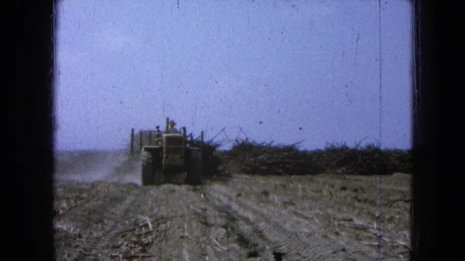 1965 Pueblo, Mexico footage shows a front-end loader moving across an arid field toward brush and debris.