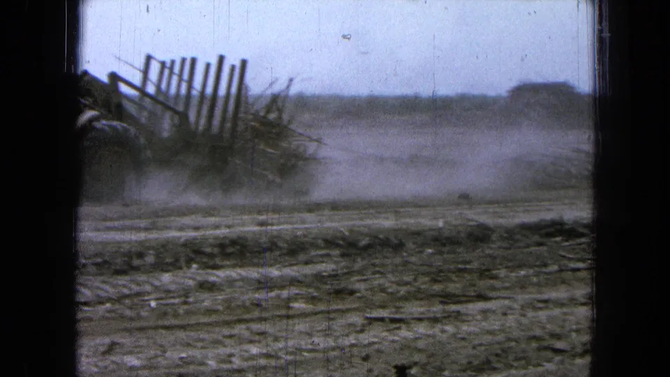 The loader is mostly at the left edge while a broad dust cloud drifts over the dirt field and distant low hill.