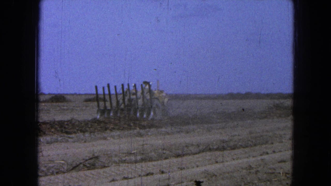 The tractor continues across the dry Pueblo, Mexico field, partly obscured by dust beside a leaning fence line.