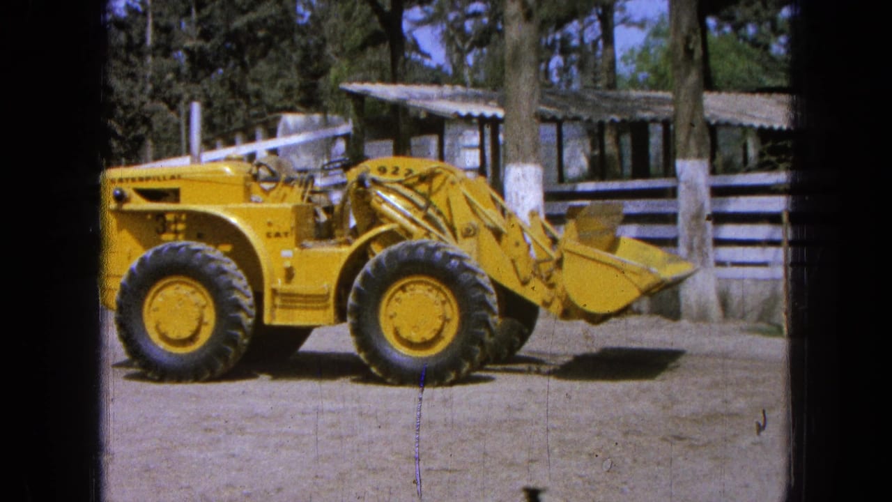 1965 Pueblo, Mexico footage shows a yellow Caterpillar front-end loader in profile near a white fence and corrugated-roof buildings.
