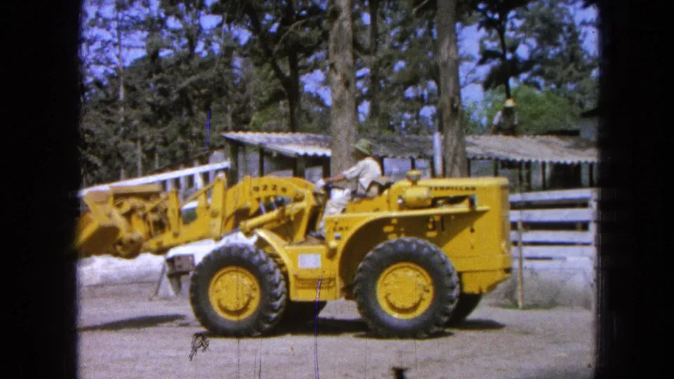 A worker continues operating the yellow Caterpillar loader in Pueblo, Mexico, with the bucket raised in a fenced outdoor yard.