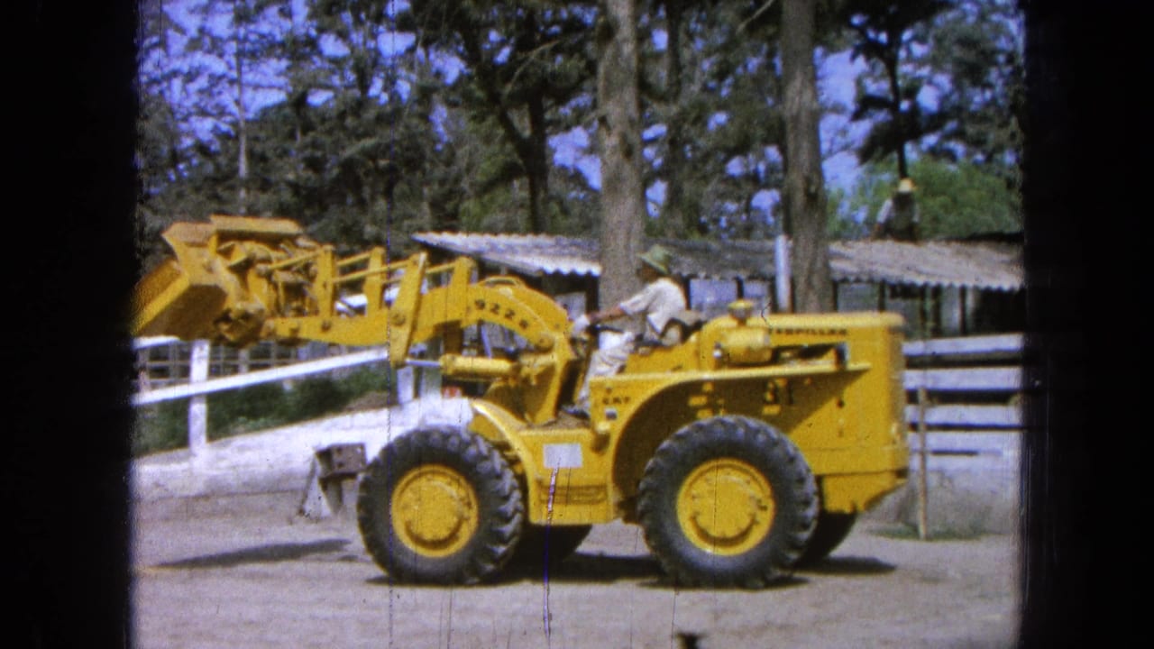1965 Pueblo, Mexico frame showing the yellow Caterpillar loader with its bucket partly raised while the operator remains seated.