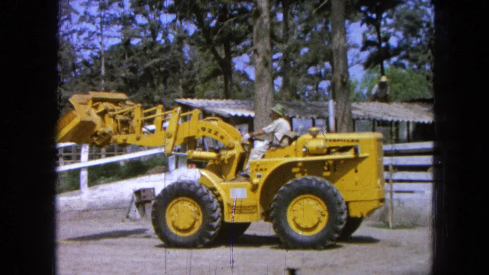1965 Pueblo, Mexico frame showing the yellow Caterpillar loader with its bucket partly raised while the operator remains seated.
