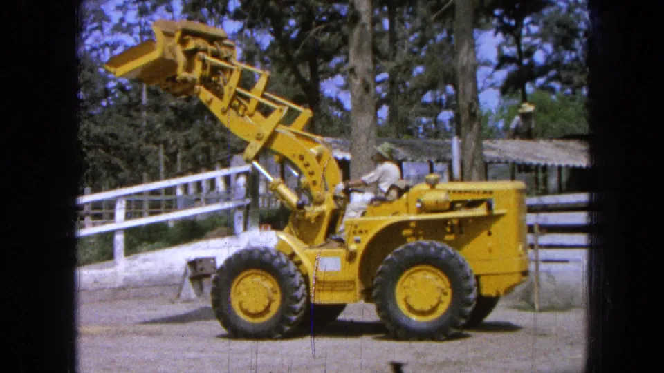1965 Pueblo, Mexico frame with the loader bucket raised high above the front tires in a ranch work area.