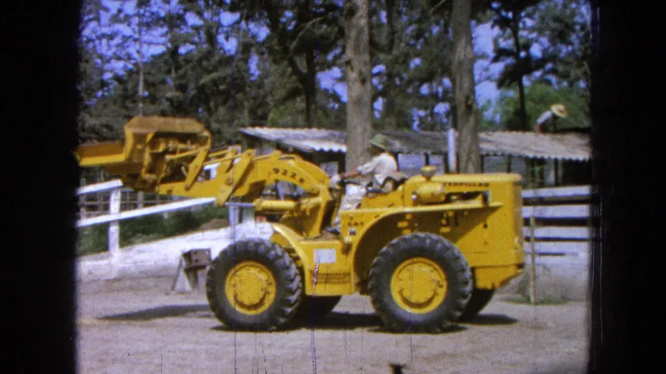 At the end of the clip, the yellow loader's bucket is lowered closer to the body while the seated operator remains visible outdoors.