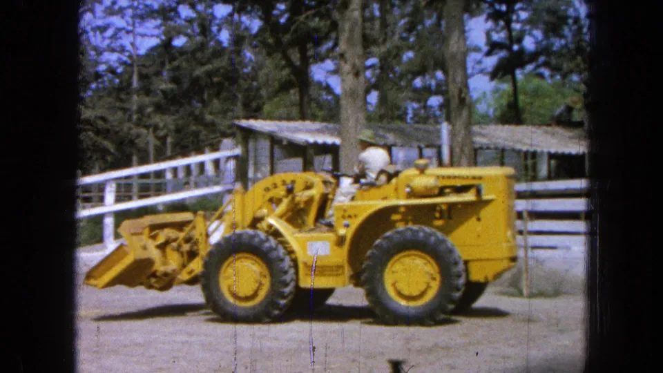 1965 Pueblo, Mexico 8mm still showing the loader bucket lowered while the operator sits above the front wheels.