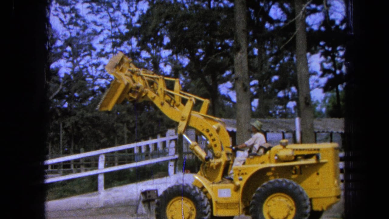 Front-end loader beside a white fence with its bucket lifted above the cab.