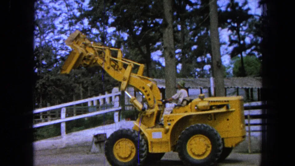 1965 Pueblo, Mexico home-movie frame showing the loader from the side as the bucket angle appears lower, with the operator and fence still visible.