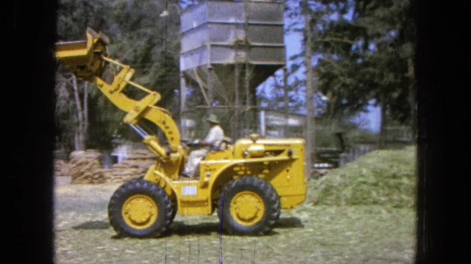 At the end of the clip, the yellow loader sits with its bucket raised on a rural Pueblo, Mexico farm, with a silo and trees behind it.