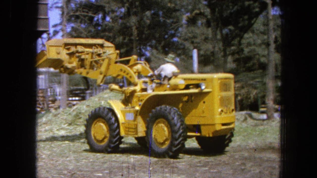 The yellow loader is seen from the side and rear as the operator maneuvers near a mound of cut grass in Pueblo, Mexico.