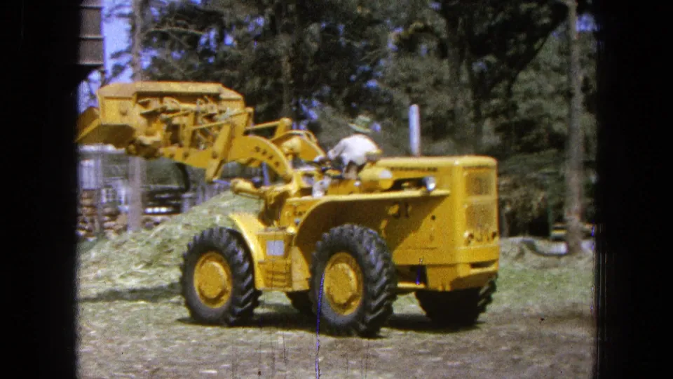 The yellow loader is seen from the side and rear as the operator maneuvers near a mound of cut grass in Pueblo, Mexico.