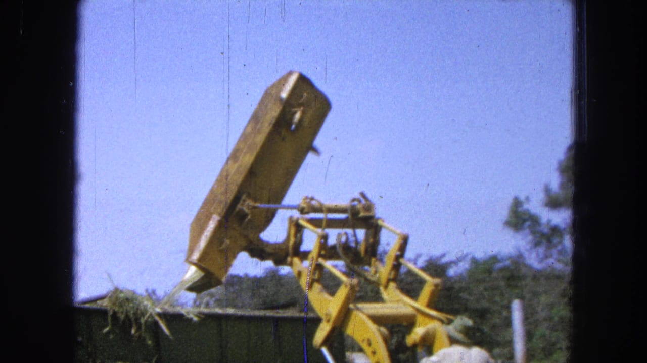Loader bucket tilts over a container as loose green material begins to fall.