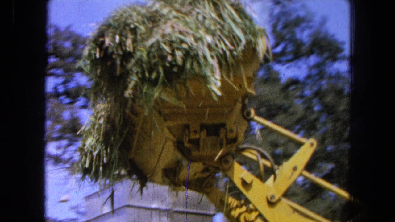 The yellow farm machine appears closer as its bucket carries hay or straw in 1965 Pueblo, Mexico home-movie footage.