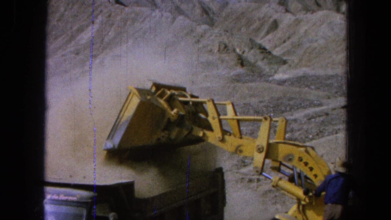 1965 Pueblo, Mexico 8mm frame with a yellow loader dumping dirt into a truck and a worker in a blue shirt near the equipment.