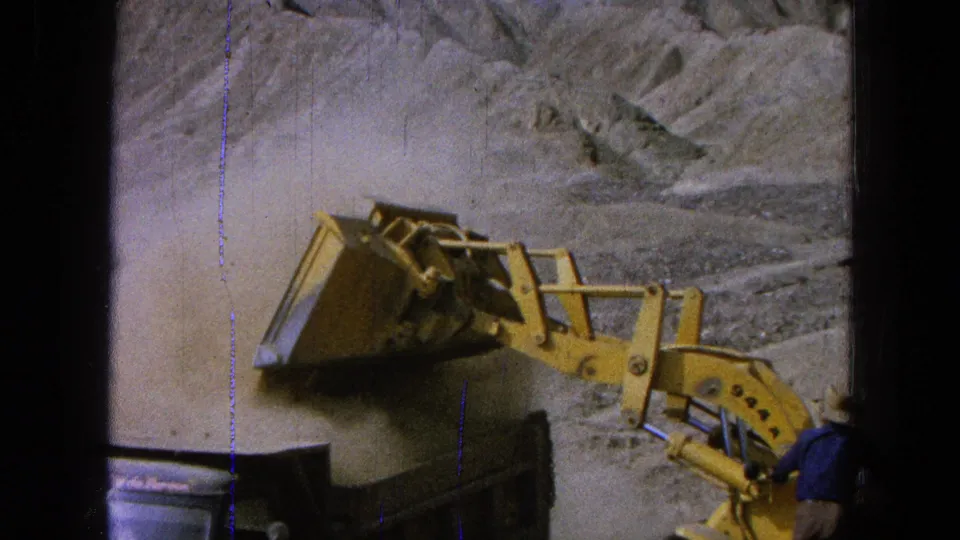 1965 Pueblo, Mexico 8mm frame with a yellow loader dumping dirt into a truck and a worker in a blue shirt near the equipment.