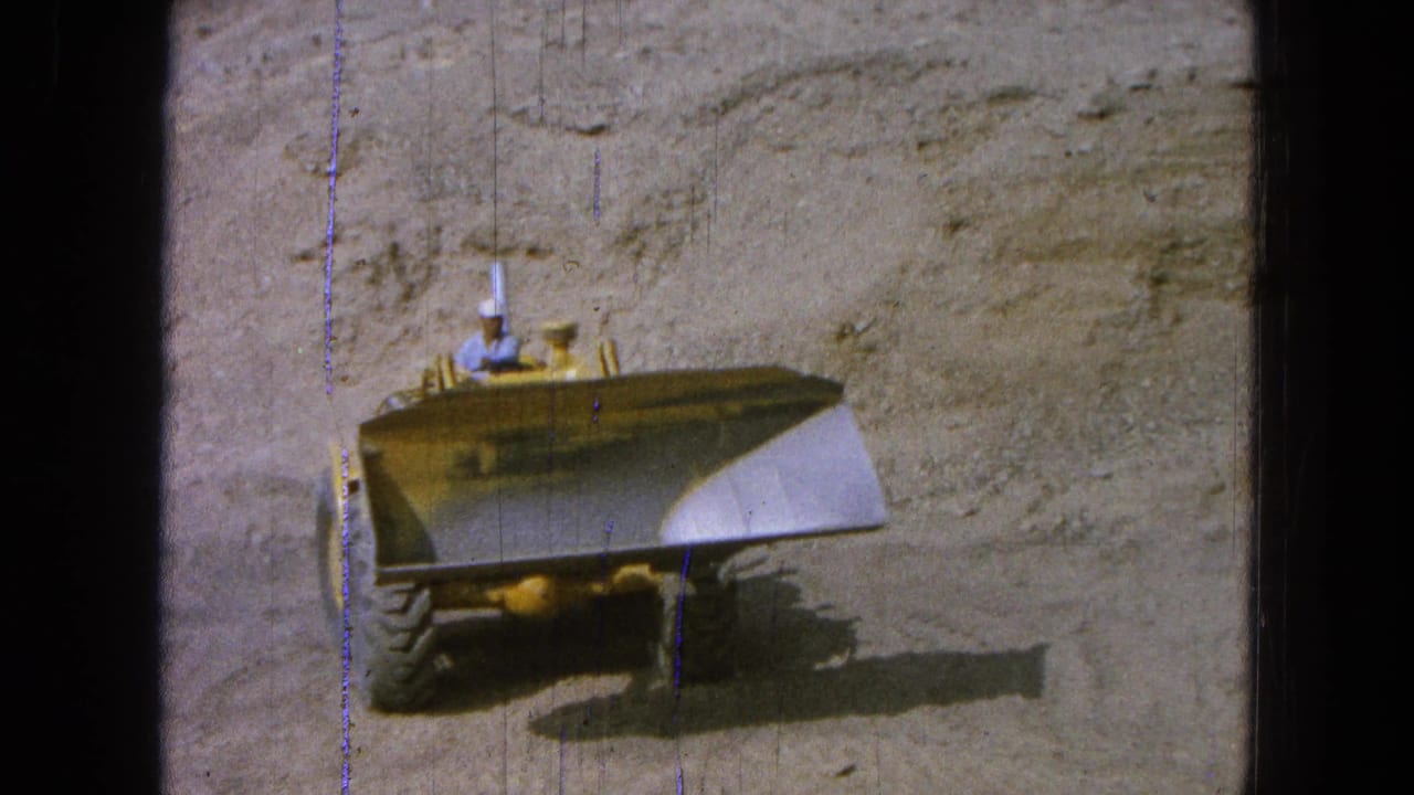 Yellow front loader approaches a sandy excavation wall with a hard-hatted operator visible.