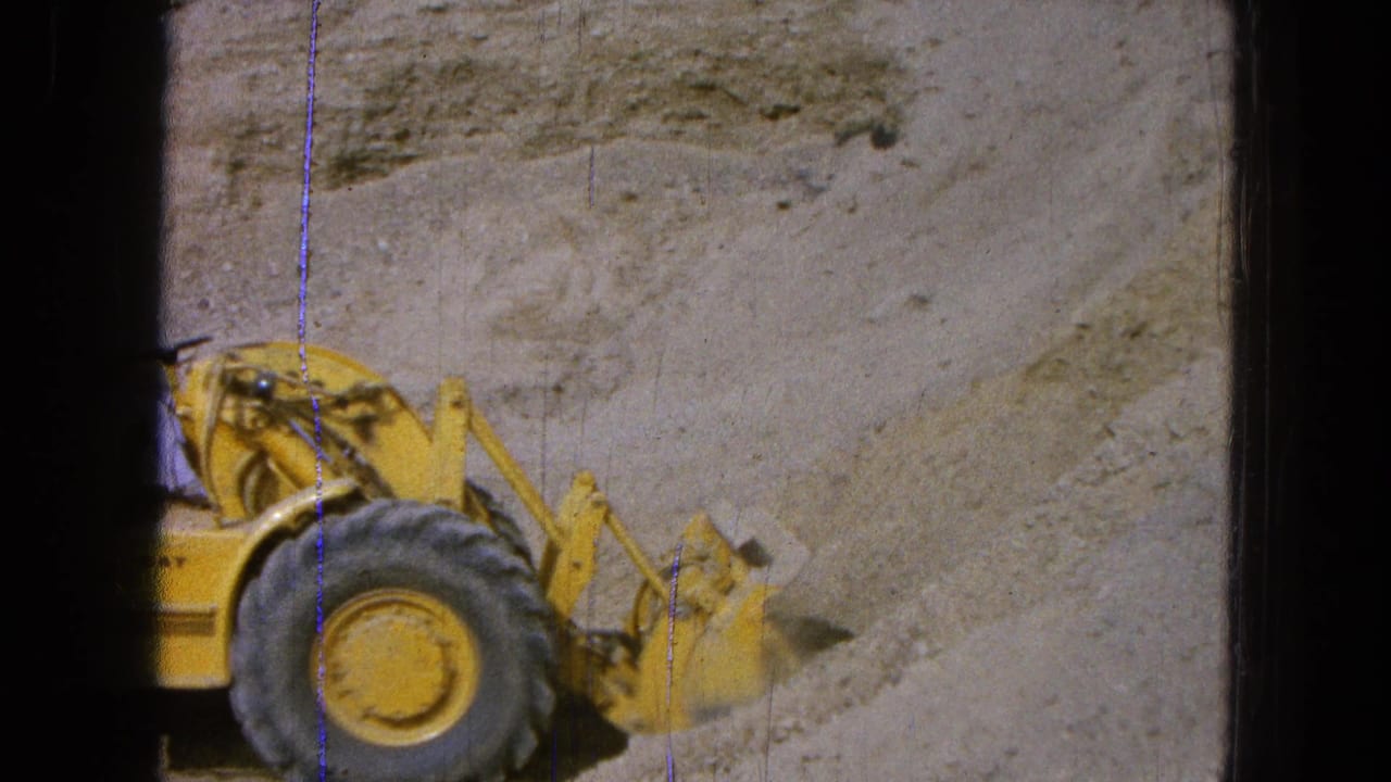 Yellow front-end loader partly visible beside a sandy excavation wall.