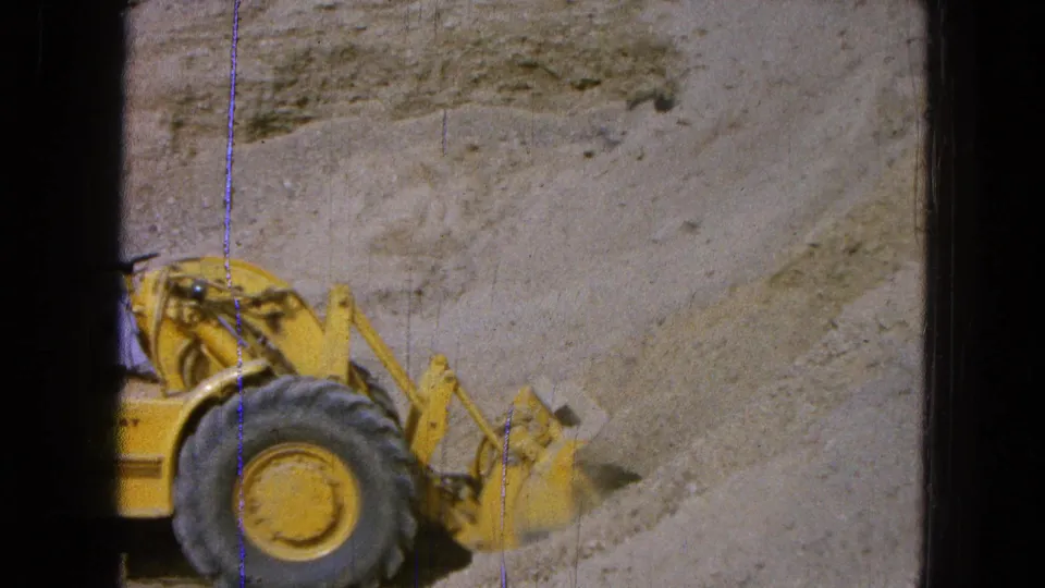 1965 Pueblo, Mexico home-movie frame showing part of a yellow Caterpillar loader working near a sandy cut bank.