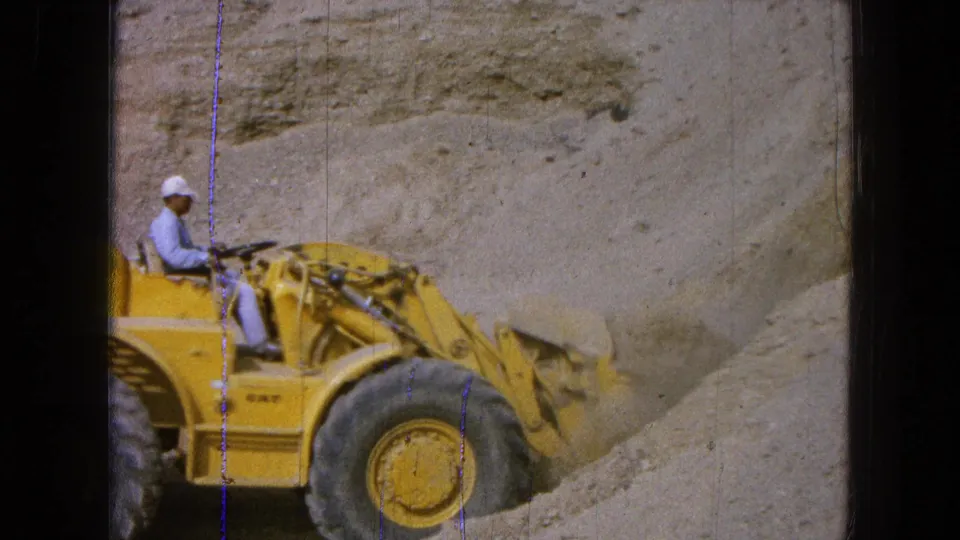 1965 Pueblo, Mexico frame showing a worker operating a yellow Caterpillar loader with its bucket near loose earth.